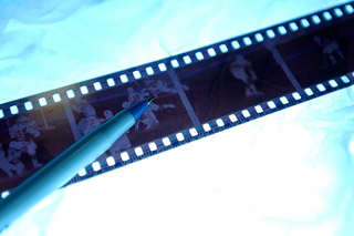 A photograph of a pen sitting on top of photo negatives, lit from behind.