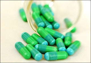Blue and green antibiotic capsules spilling out of a cup.
