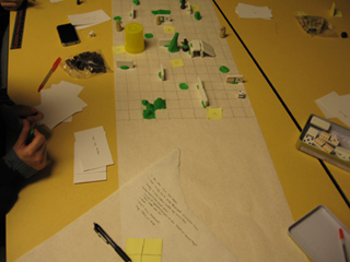 A paper grid with various obstacles of Play-Doh and dominos functions as a board for a game with tokens and dice.