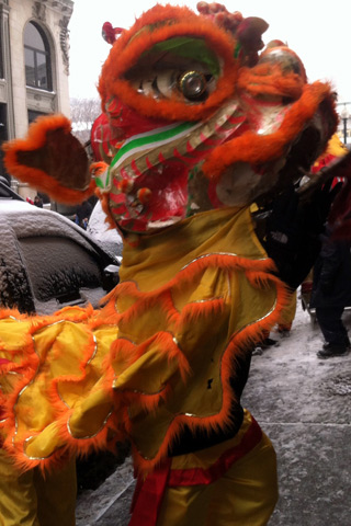 A photograph of a red, orange, and yellow Asian dragon costume on a snowy city street