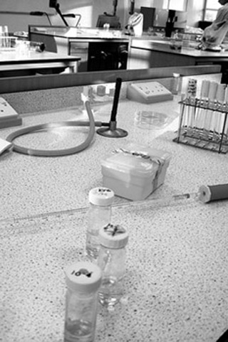 Black and white photo of lab counter with three vials of bacterial cultures and other lab equipment.