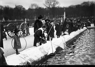 Photo of children in Luxembourg playing with toy sailboats on a pool in a public garden.