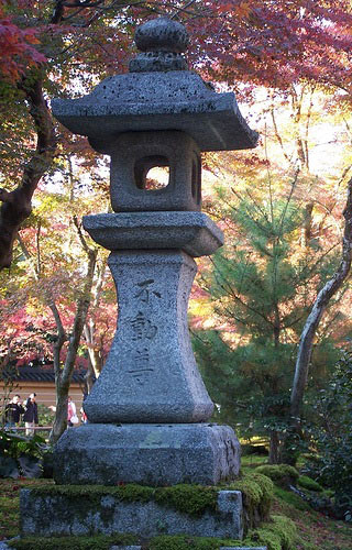 A photo of trees in the autumn and a small obelisk shaped stone with Japanese carved into it.