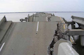 Photo of collapsed concrete bridge roadway over water.