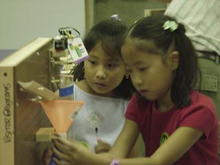 A photo of two girls creating a path for a falling ball on a peg board.