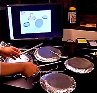 Photo showing hands playing four foil “drums” wired to a computer, with the Scratch cat character animated on screen.