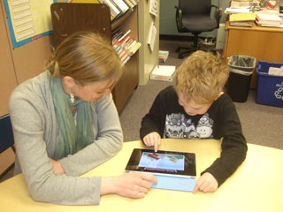 A photo of an autistic boy using an iPad with his teacher.